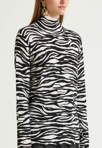 Maglione dolcevita a maniche lunghe a righe zebrate in bianco e nero, caratterizzato da una texture morbida e un design aderente.