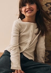 Haut beige clair à manches longues côtelé avec des boutons sur le devant, associé à un jean en denim bleu foncé. Tissu texturé et coupe décontractée.