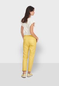 Pantalons en simili cuir jaune avec une coupe fuselée, taille élastique et poches au dos, associés à un haut blanc à manches courtes avec des manches volantes.