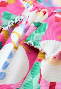 Vestido multicolor que presenta tela a rayas rosas y blancas, con patrones de hojas verdes y azules. Puños con volantes y dobladillos redondeados que añaden textura.