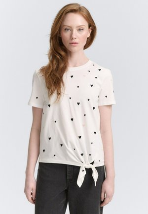 Weißes T-Shirt mit kurzen Ärmeln, verziert mit schwarzen und rosa Herzmustern, das vorne geknotet ist für einen maßgeschneiderten Look.