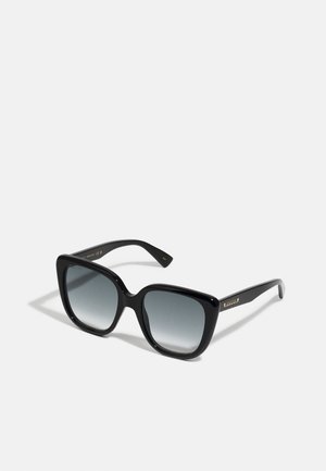 Gafas de sol de gran tamaño en color negro con lentes degradados. Acabado brillante, montura cuadrada y logotipo dorado en la patilla. Diseñadas para protección UV.