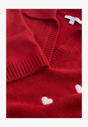 Červený pletený svetr s výstřihem do V, žebrovaným límcem a bílou výšivkou srdce u lemu. Měkká textura a lehký vzhled.