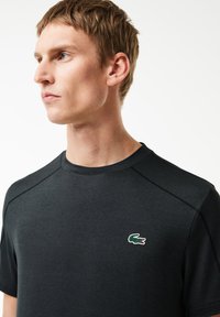 T-shirt nera a maniche corte con colletto tondo, adornata da un logo di coccodrillo verde e rosso sul petto e dettagli di cucitura discreti.