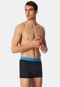 Svarta boxerkalsonger med en blå elastisk midje, som har en tajt passform och mjuk textur. Midjebandet har varumärket "SCHIESSER" präglat.