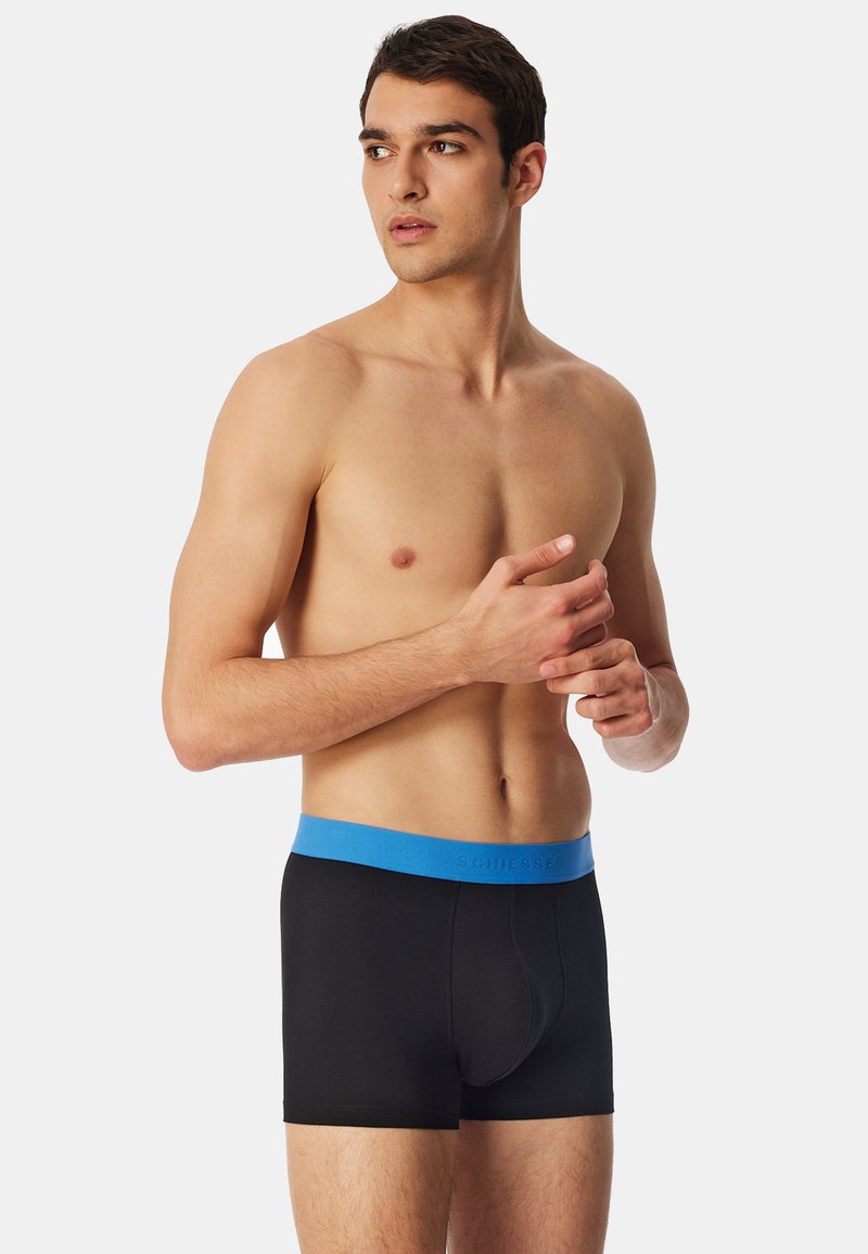 Svarta boxerkalsonger med en blå elastisk midje, som har en tajt passform och mjuk textur. Midjebandet har varumärket "SCHIESSER" präglat.
