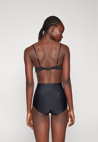 Ensemble de lingerie noire comprenant un soutien-gorge simple avec des bretelles ajustables et une culotte taille haute, fabriqué en tissu lisse avec un minimum de détails.
