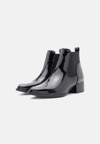 Crne lakirane Chelsea čizme s elastičnim bočnim panelima i niskim blok petama, koje imaju glatku sjajnu završnicu i zaobljeni vrh.