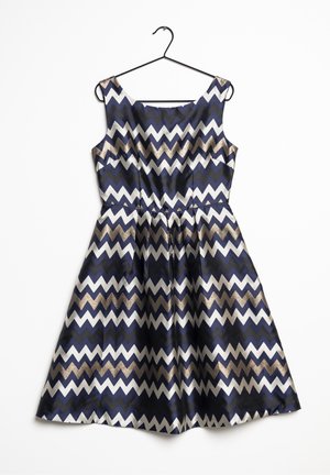 Ärmelloses Kleid mit Marineblau, Schwarz, Weiß und Gold in Zickzackmuster, tailliert mit ausgestelltem Rock, auf einem schwarzen Kleiderbügel vor weißem Hintergrund angezeigt.