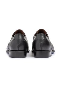 Scarpe da dress nere in pelle con dettagli brogue, caratterizzate da una finitura liscia, punta rotonda e tacco impilato. La suola presenta una leggera texture.