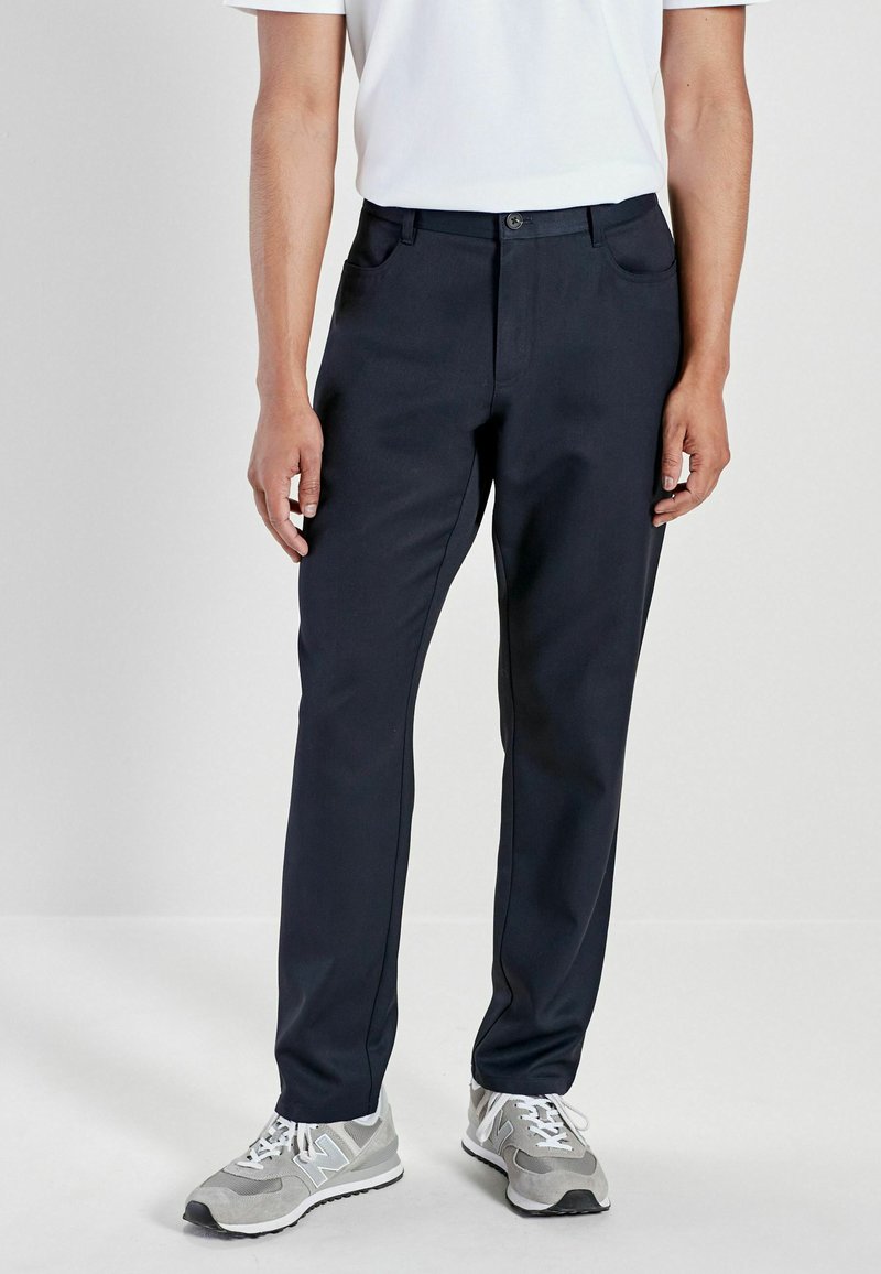 Navy blue trousers with a straight cut, made from a smooth fabric. Features front pockets and a button closure, worn with gray sneakers.