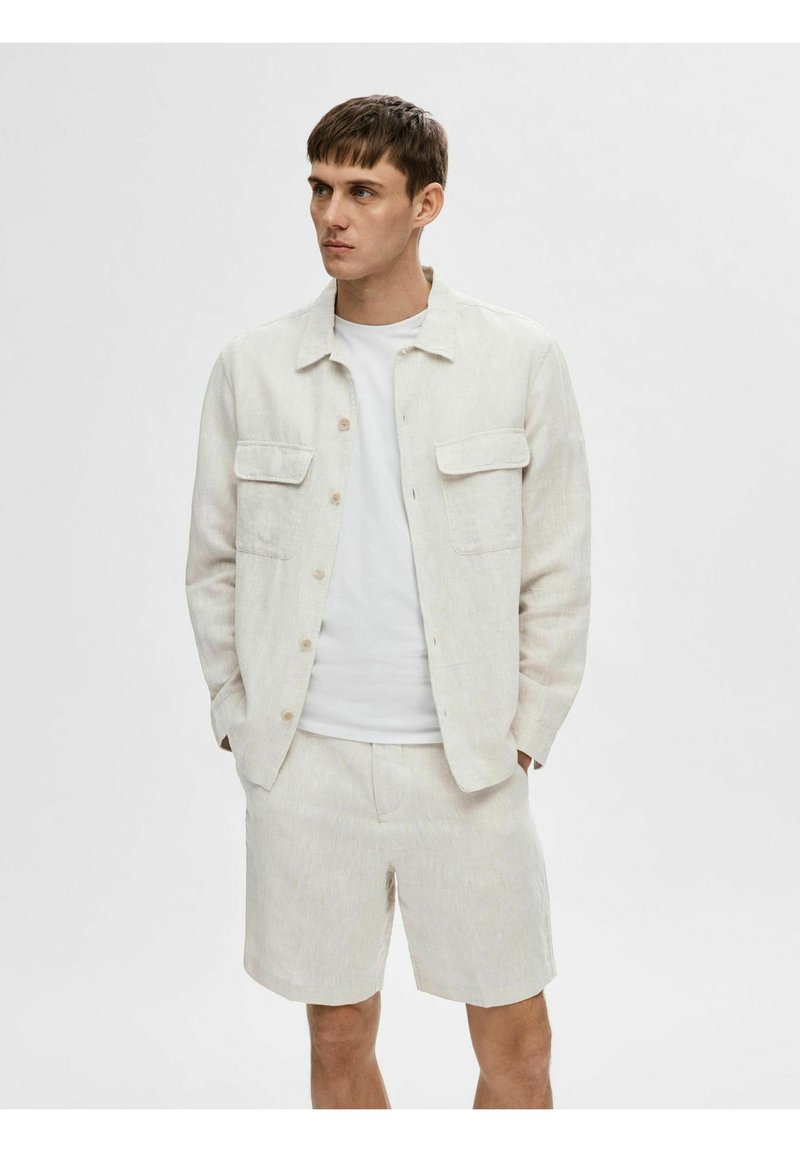 Lichtbeige linnen overhemdjacket met twee voorkruiden, gecombineerd met bijpassende shorts. De outfit heeft een eenvoudig wit T-shirt eronder.