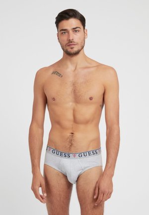 Graue Baumwollslips mit einem marineblauen und roten "GUESS"-Logo-Bund, featuring ein körperbetontes Design und glatte Textur. Modell zeigt die Vorderansicht.