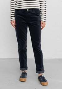 Navyblå kordflorsbyxor med slim fit, med knappstängning och uppvikta muddar, i kombination med navyblå sneakers och en randig långärmad skjorta.