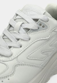 Bijela atletska cipela s teksturiranom kožom i mrežastim umetcima, s ravnim vezicama, suptilnim šavovima i zaobljenim potplatom.