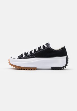 Sort lavtop sneaker med hvide snørebånd, tyk hvid platformsål og en zigzag-mønsteret brun og sort gummi ydersål.