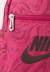 Rózsaszín hátizsák, texturált mintázattal, ezüst cipzárhúzóval és egy kiemelkedő fekete Nike logóval. Az anyaga tartónak és szintetikusnak tűnik.