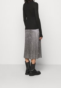 Haut noir côtelé à manches longues, jupe midi plissée argentée, et bottines noires à semelles épaisses. Tissus texturés visibles dans le design.