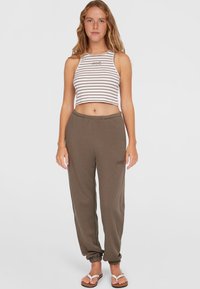 Rikkalised crop-top valgest ja pruunist, koos pruunide dressipükstega, millel on elastsed varrukad; mudel kannab valgeid sante.