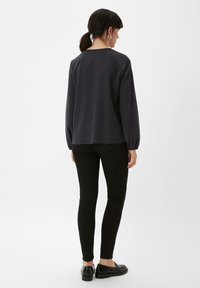 Schwarzes Langarmoberteil mit relaxed Fit, mit gerafften Manschetten und rundem Ausschnitt, kombiniert mit schwarzen Slim-Fit-Hosen und glänzenden Loafers.