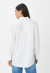 Witte blouse met lange mouwen en een klassieke kraag, geplooide achternaad en knoopsluiting. Glad materiaal met een ontspannen fit en een gebogen zoom.