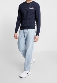 Marinblå sweatshirt med lång ärm och logotyp, kombinerad med ljusblå jeans och vita sneakers, med en avslappnad passform och ribbade ärmslut.