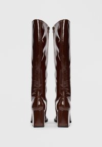 Botas de couro patente castanhas até ao joelho com um design elegante, saltos quadrados e costuras verticais, apresentando zíperes na parte de trás.