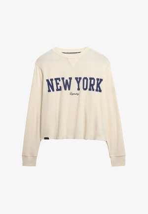 Kremowy, krótki sweter z prążkowanej tkaniny, z nadrukiem "NEW YORK" w kolorze granatowym oraz logo "Superdry" poniżej. Luźny krój.
