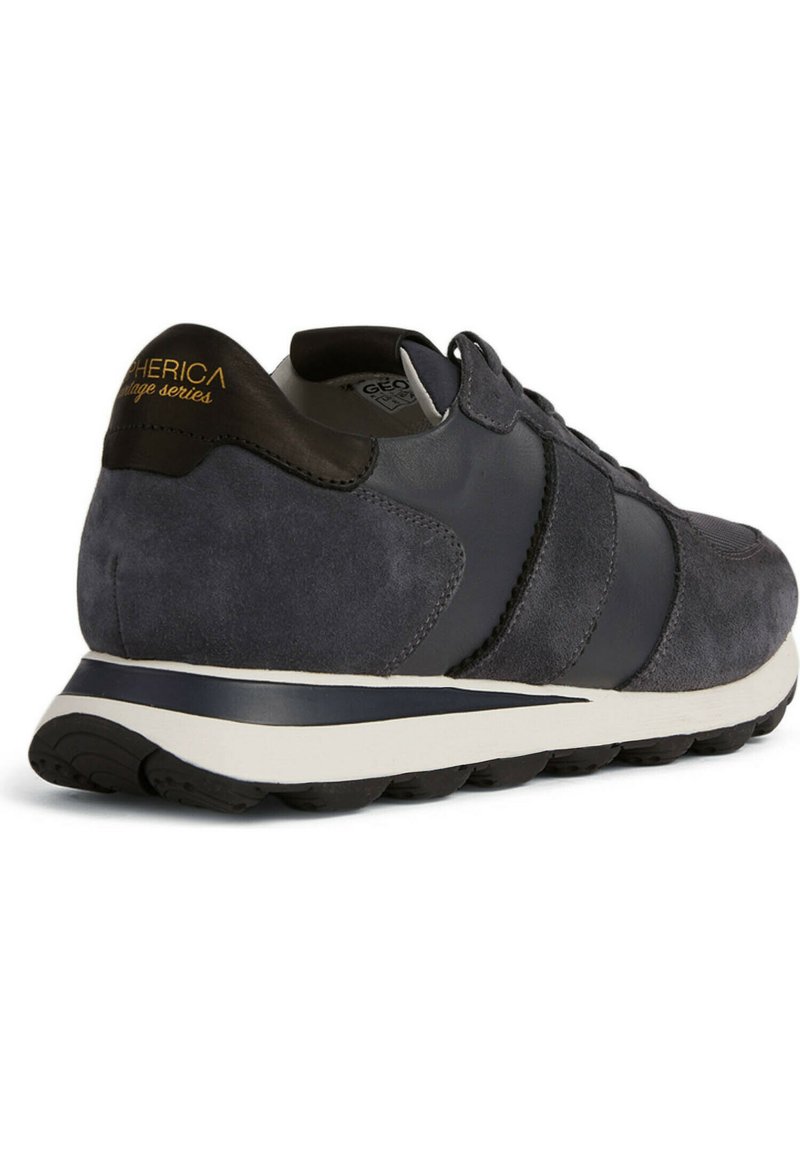 Sneaker in suede grigio con accenti in pelle blu navy, suola bianca e distintivo logo giallo sul tallone, caratterizzato da un design sportivo e superficie testurizzata.