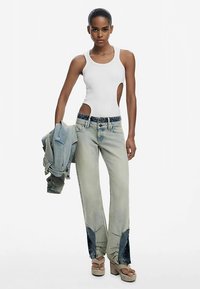 Bílý top bez rukávů, světlé džínové kalhoty s tmavě modrými detaily, vrstvená džínová bunda a béžové platformové boty. Hladké a přiléhavé materiály.