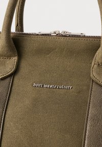 Olijfgroene canvas handtas met een ritsclosure, voorzien van een gestructureerd oppervlak en zilveren tekstdetail "verspil cultuur niet".