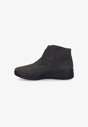 Bottine en daim gris avec une sangle Velcro, un bout effilé et une semelle en caoutchouc noir texturé avec un motif strié pour l'adhérence.