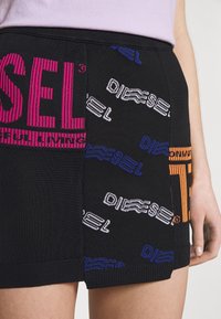 Zwarte rok met een mix van geweven texturen, gedurfde logo-ontwerpen in roze, blauw, wit en oranje, met een geribbelde tailleband.