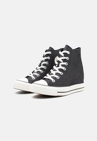 Zwarte hoge sneakers met een textiel bovenwerk, witte veters, rubberen neuskap en een zwart-witte gestreepte zool.