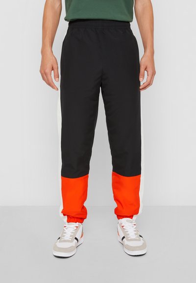Pantalon de survêtement noir avec des accents orange et blanc, taille élastique et poignets ; fabriqué à partir d'un matériau lisse et léger.