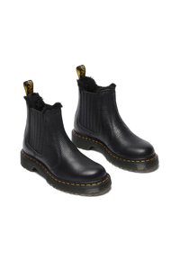 Botas Chelsea de cuero negro con acabado texturizado, forro de suave pelaje, paneles laterales elásticos y costuras amarillas en la suela de goma.