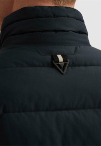 Πίσω μέρος ενός μαύρου επενδυμένου μπουφάν με ψηλό γιακά, με μαύρο τρίγωνο κλιπ και χρωματιστό υφασμάτινο λουρί.