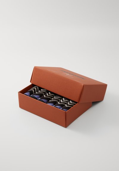 Cutie de șosete cu un design texturat, având modele zigzag în culorile negru, albastru și alb. Cutia este portocalie, cu un logo imprimat.