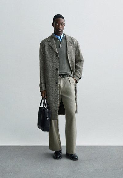 Sivi kaput s ribanim uzorkom, maslinasti pulover, svijetloplava košulja s ovratnikom, bež hlače, crni pojas s okruglim detaljima, crna torba, sjajne cipele.