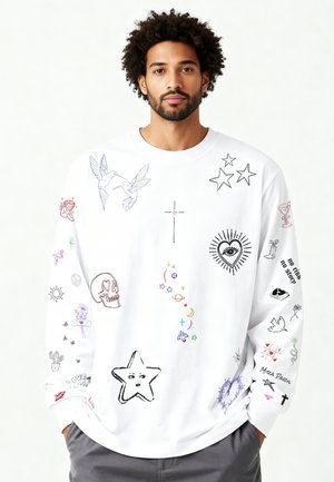 Man met krullend haar die een witte sweatshirt draagt met kleurrijke tekeningen van sterren, schedel, vogels, een hart met oog, kruis en de tekst "no risk no story".