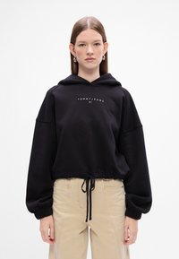 Felpa nera corta realizzata in materiale morbido, con orlo regolabile, maniche oversize e logo "TOMMY JEANS" sul frontale.