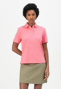 Korte mouwen roze polo-shirt met een kraag, voorzien van drie knopen en een klein logo. Gecombineerd met een kaki rok met voorzakken.