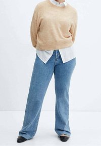 Beige verkürzter Pullover über einem gestreiften Shirt in Weiß und Blau, kombiniert mit hellblauen Schlagjeans und schwarzen spitzen Ballerinas.