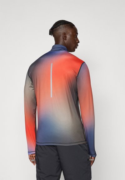 Camisa deportiva de manga larga con un degradado de rojo a azul, fabricada con material ligero, con una textura geométrica y detalles reflectantes.
