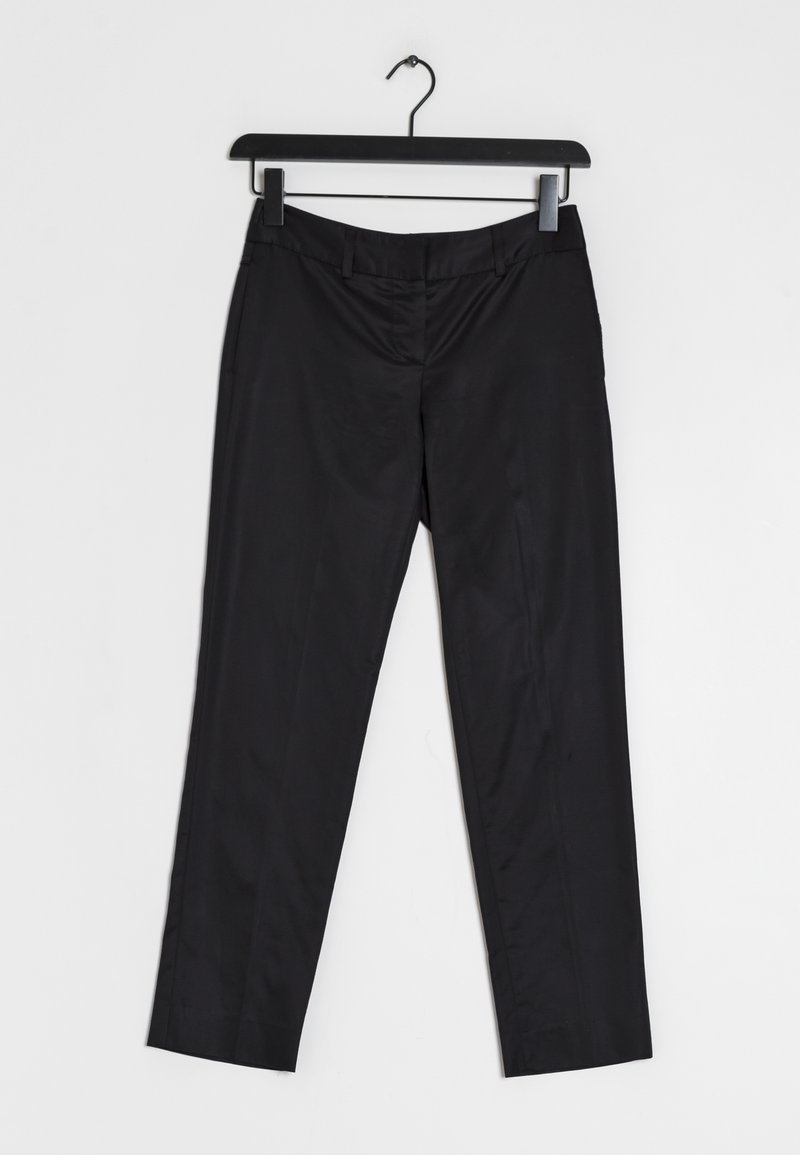 Pantalons noirs taillés suspendus à un cintre noir sur fond blanc, dotés de passants pour ceinture et d'une fermeture éclair frontale.