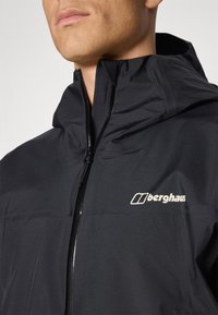 Black waterproof jacket with a high collar, front zipper, and textured fabric. Features a prominent "Berghaus" logo in white.