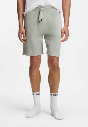 Mand iført lysegrå strukturerede strikkede shorts med frontlommer, en snøre i taljen, hvide sokker med sort "BOSS" tekst og en hvid skjorte.