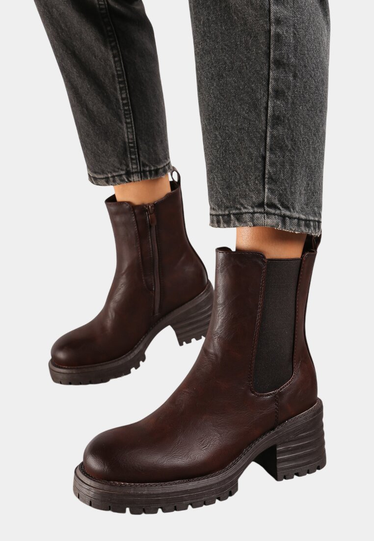 Bottines en cuir marron avec une finition texturée, des panneaux latéraux élastiques et des talons en caoutchouc épais. Portées avec un jean noir à revers.