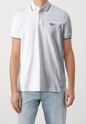 Mężczyzna noszący białą koszulkę polo z krótkim rękawem z czarnym obszyciem i logo „JOOP! JEANS”, w połączeniu z jasnoniebieskimi dżinsami.