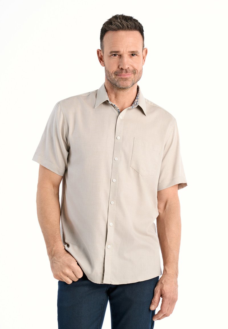 Camicia beige a maniche corte con colletto a bottoni, caratterizzata da un colletto interno a fantasia e una tasca sul petto. Realizzata in tessuto liscio.